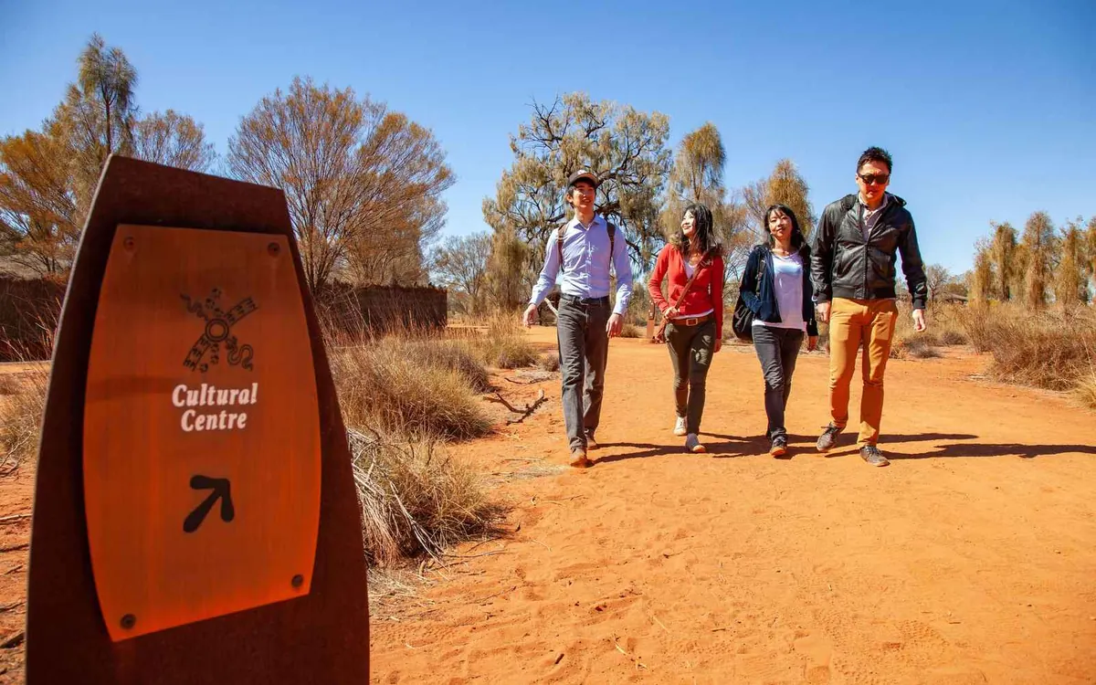 A shaded walking path beside the Uluru-Kata Tjuta Cultural centre with desert plants on both sides and red earth underfoot