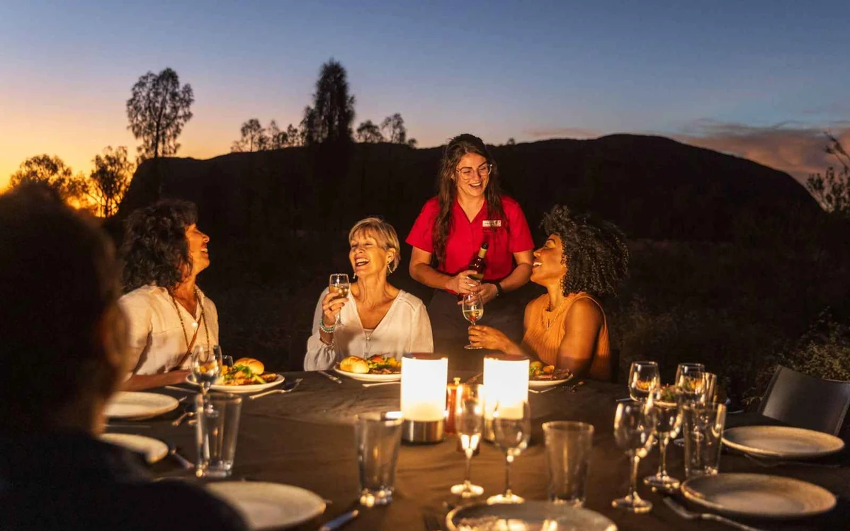 People eating at an outdoor BBQ dinner in the desert after dark near Uluru