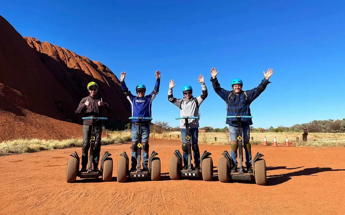 Segways parked on a track beside the red rock face of Uluru
