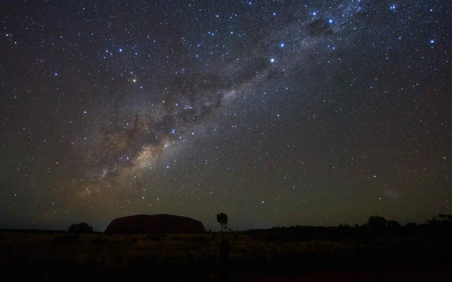 A telescope pointed at the night sky in the desert with the horizon barely visible