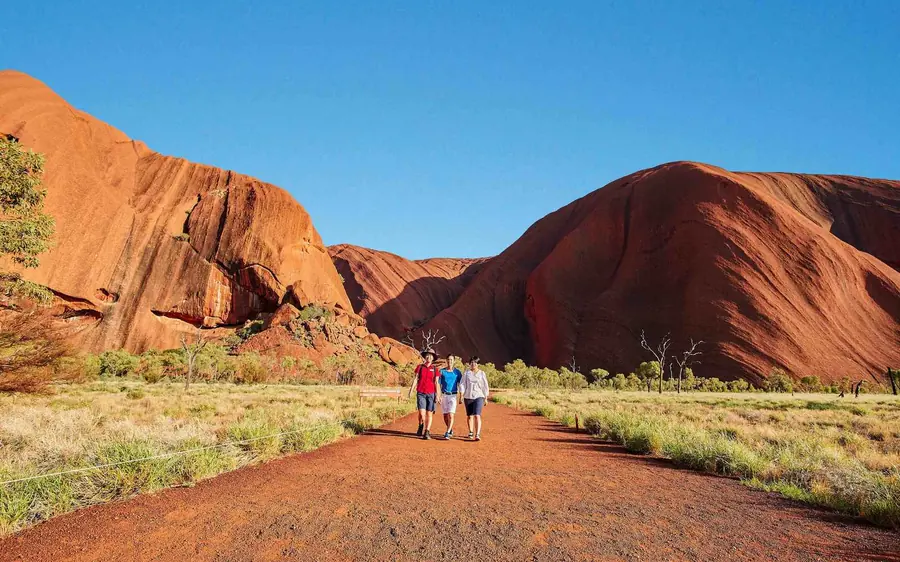 A waterhole at the foot of the red rock wall of Uluru with green trees around it