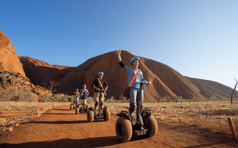 Segways parked on a sandy track beside the red rock face of Uluru