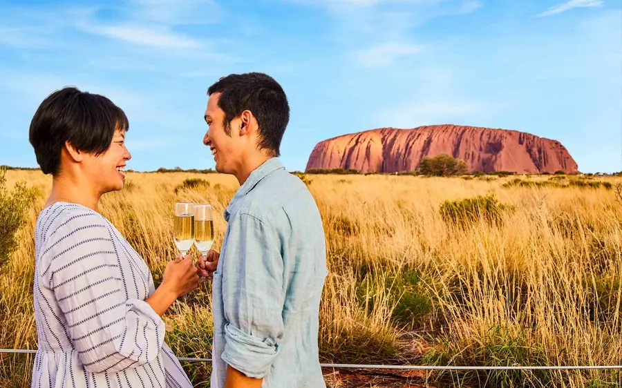 Glasses of sparkling wine on a table in the desert with Uluru on the horizon