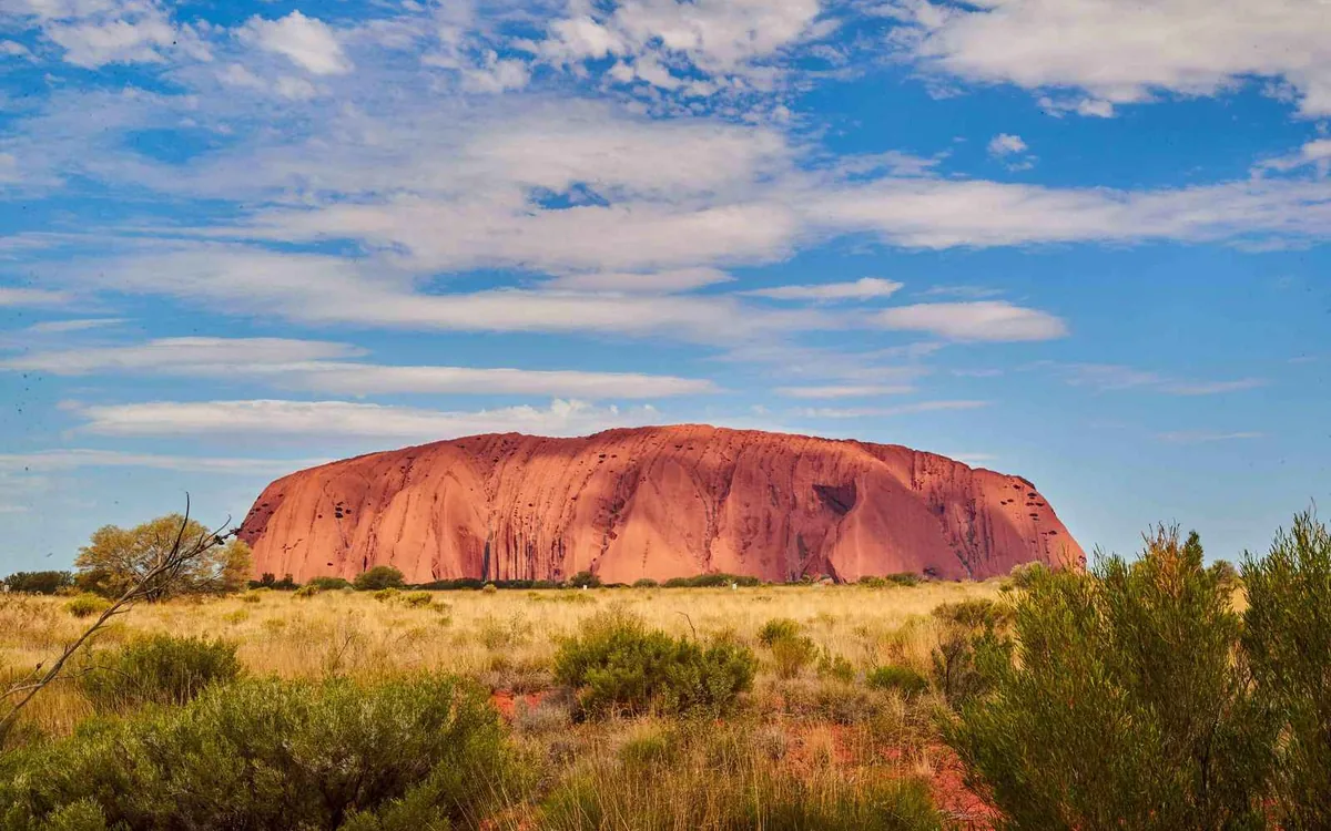 Uluru standing alone above red sand and spinifex under a clear sky in the Northern Territory