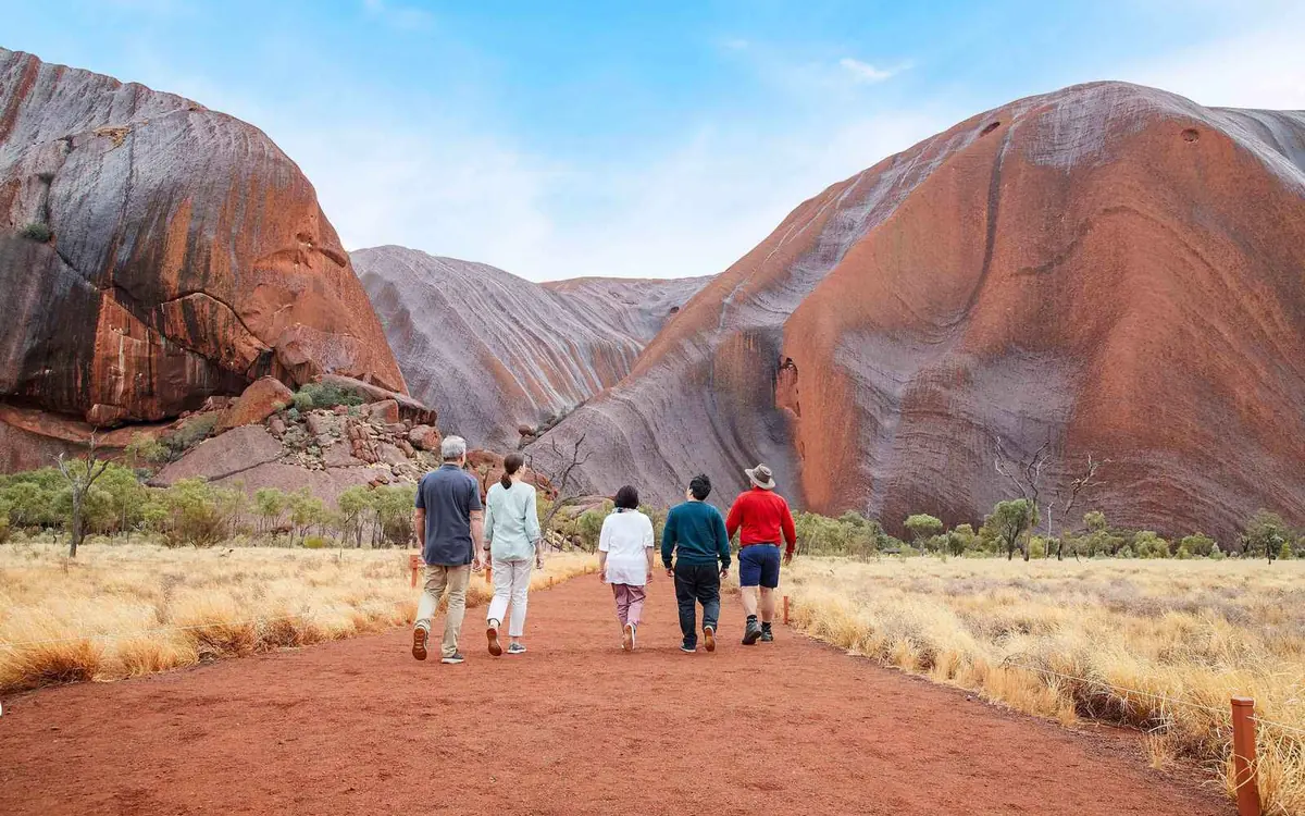 A walking track running along the foot of the red rock face of Uluru